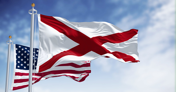 United States and Alabama flags waving together on a sunny day. The flag of Alabama features a red cross on a white field. 3d illustration render, Fluttering fabric. Selective focus