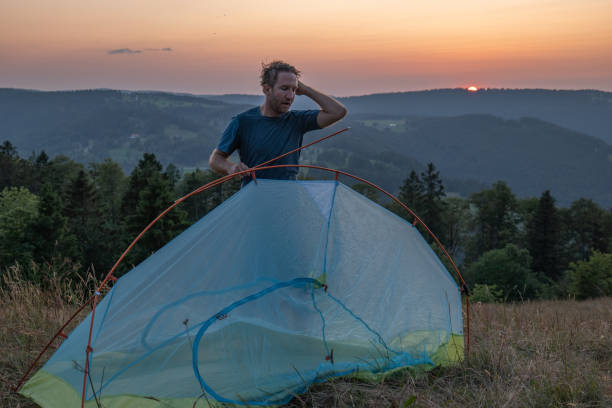 istock Man camping in summer sets up a tent at sunset 1591885266