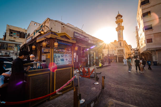View of the Almaghrabi Masjid Mosque (Al Maghrabi Masjid Mosque) at the historic district Al Balad in Jeddah, KSA, Saudi Arabia Al-Balad, Jeddah, Saudi Arabia - March 16th 2023: In the heart of the old town of Al-Balad, time seems to have stopped. Next to the dilapidated ruins of better days gone by, the townhouses, magnificently renovated in the course of the Saudi royal family's Vision 2030, rise from the hustle and bustle of the city. Small stalls that are not part of the souk can be found everywhere. The minaret of the Al Maghrabi Masjid mosque rises in the background. Plenty of people visible. jeddah stock pictures, royalty-free photos & images