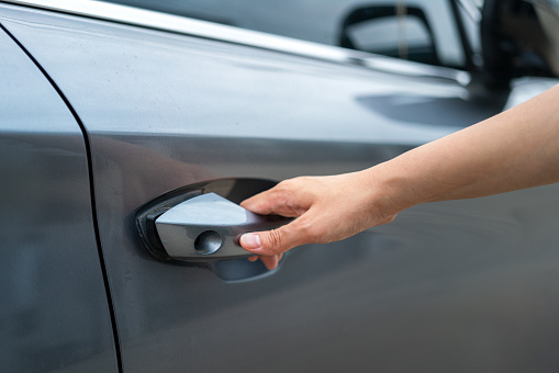 Action of a car driver hand is unlocking and opening the door to entry into the car. Close-up and selective focus on hand's part.