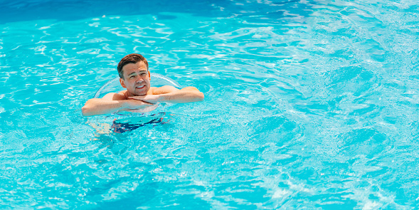 Season of sunbathing and enjoying by the pool. Feel the sun and music by the pool. A handsome man is refreshing in the water in the pool and listening to a song Resting and enjoying sun and summertime