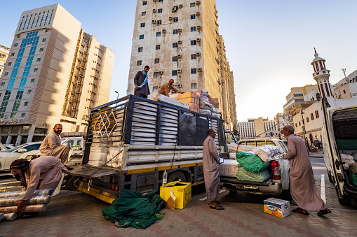Al-Balad, Jeddah, Saudi Arabia - March 16th 2023: Outside the imaginary border of Al-Balad, men load a truck and a pick-up truck with rolls of fabric they have just bought in one of the many textile and fabric stores in Al-Balad.