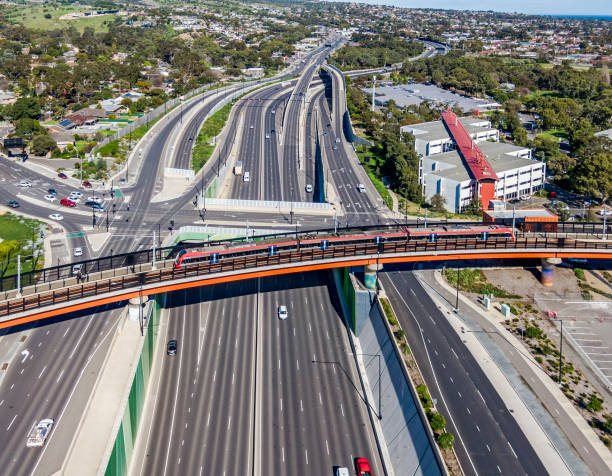 istock Aerial view modern electric train on bridge over multi-lane highway with intersection, interchange in treelined suburb 1591915983