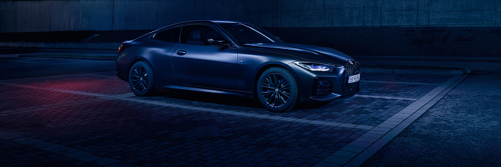 Black BMW 4 series coupe in an empty parking lot in front of Arena Gliwice sports hall at night. Poland, February 19, 2023