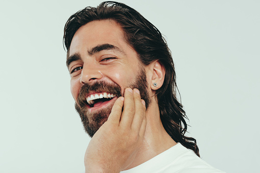 Portrait of a happy young man smiling in a studio, looking at the camera with confidence as he proudly rocks a beard, long hair and radiant skin. Man embracing a lifestyle of grooming and self-care.