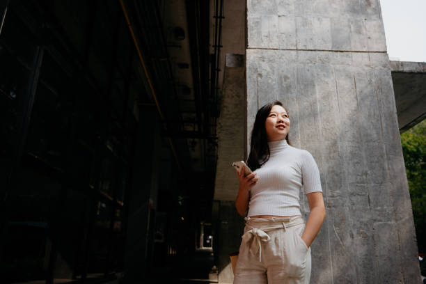 istock Asian woman using smartphone in front of a modern office building 1591937945
