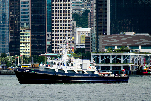 A patrol boat of the Hong Kong Police sails on Victoria Harbour.  In the background is a Star Ferry and pier.  This image was taken from Tsim Sha Tsui, Kowloon on a sunny afternoon on 6 July 2023.