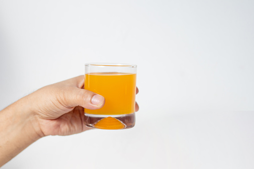 The person's hand is holding an orange water glass against a white background.