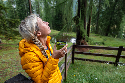 Woman bikepacking and camping, she drinks her coffee in the morning under a wooden shelter