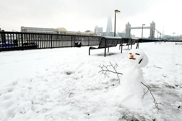 Snowman by the river Thames, with Butlers Wharf to the left of the image, and Tower Bridge, the Shard building and City Hall in the background, Wapping Borough of Tower Hamlets, East London, England, UK