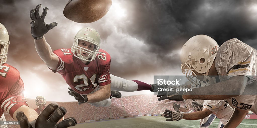 American Football Action american football player in mid air about to catch ball in professional game in floodlit stadium under stormy sky at sunset American Football - Sport Stock Photo