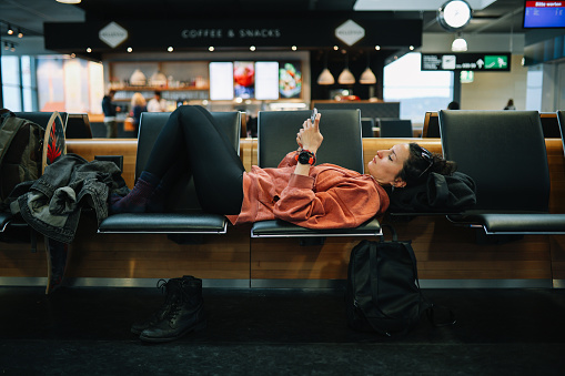 Woman relaxing at the airport, reading stuff on her smartphone, having a long layover.
