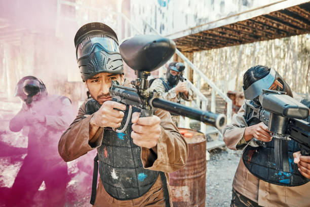 istock Teamwork, shooting and paintball with man in game for playground, war and gaming. Challenge, mission and soldier with people and smoke in battlefield arena for target, gun and warrior training 1592049829
