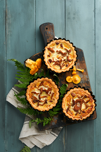 Savory hands pie with chanterelle mushrooms, cream and cheese on cutting board on rustic old wooden table background. Homemade tarts with seasonal chanterelle mushrooms. Rustic style. Top view.
