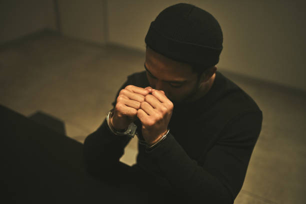 istock Interrogation, worry and criminal with handcuffs in jail for investigation, stealing and theft in station. Arrested suspect, law and man praying with anxiety, worry and scared in prison for crime 1592106924