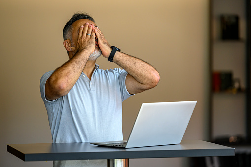 Portrait of a desperate mature businessman standing at a table reading at his laptop