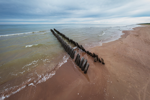 Old fishing boat pier wooden poles near Koshrags. Baltic sea can be seen in the background