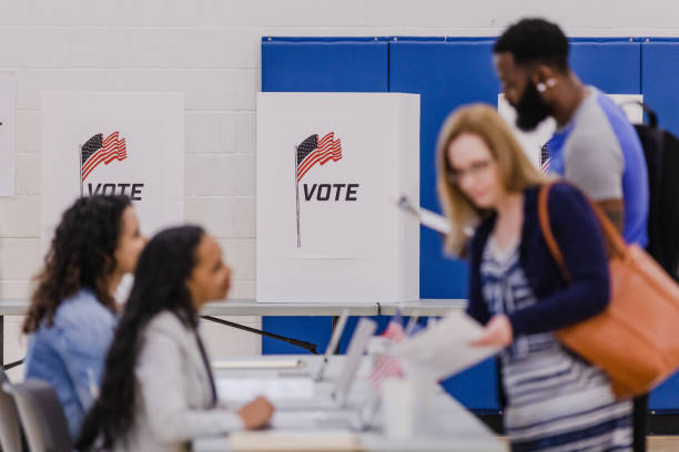 istock Focus on voting booth with voters and volunteers in foreground 1592133759