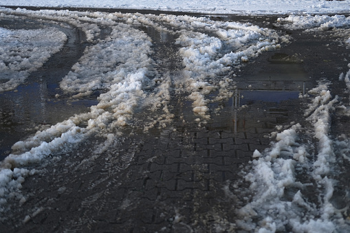 part of street in city, pavement after heavy snowfall, wet snow melts, puddles, slush and mud impede movement of pedestrians and vehicles, concept traffic safety, work of public utilities