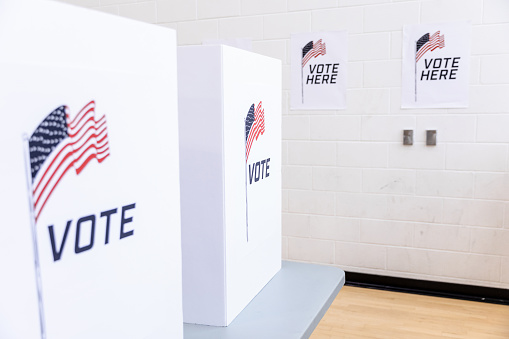 Two voting booths and signs on the wall at the polling place are decorated with American flags.