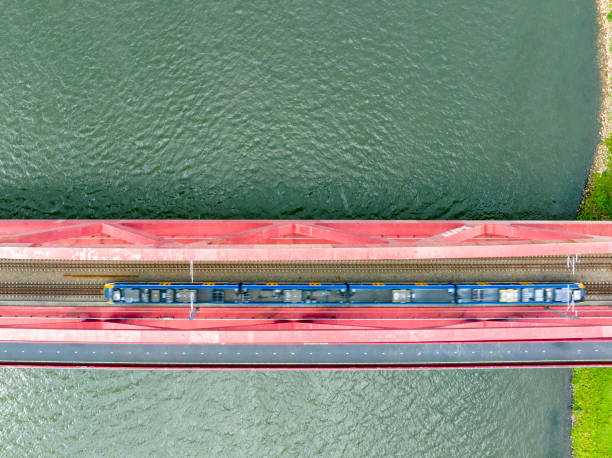 istock Railroad tracks on a railway bridge over a river with a train passing seen from above 1592139670