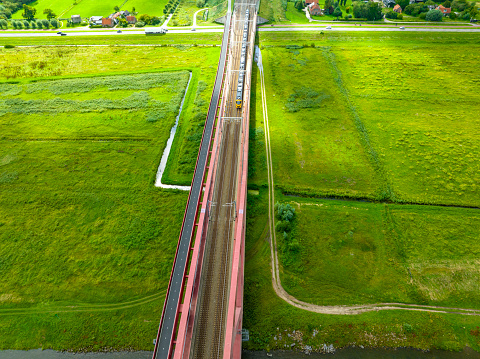 Railroad tracks on a railway bridge over a river and road with a train passing seen from above from a high viewpoint.