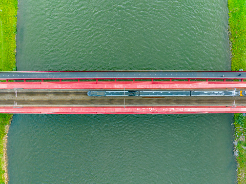 Railroad tracks on a railway bridge over a river with a train passing seen from above from a high viewpoint.