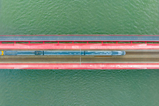 istock Railroad tracks on a railway bridge over a river with a train passing seen from above 1592140903