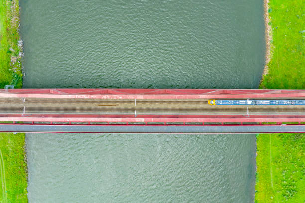 istock Railroad tracks on a railway bridge over a river with a train passing seen from above 1592142059