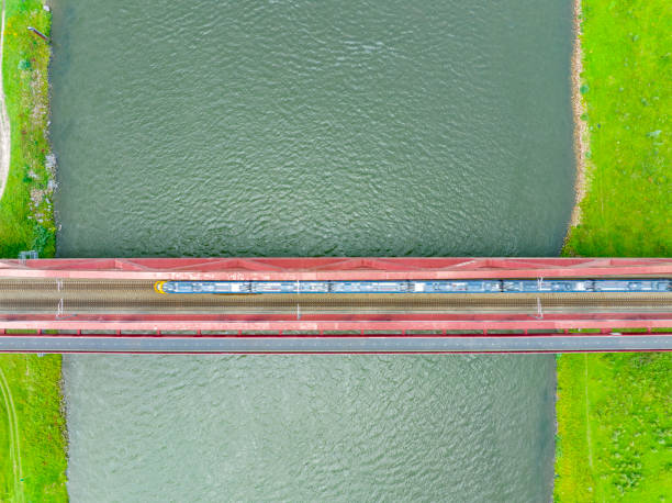 istock Railroad tracks on a railway bridge over a river with a train passing seen from above 1592143215