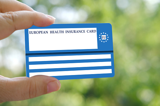 European insurance healthcare card in female hand on natural green background, EU document healthcare support, medical expenses, emergency, healthcare safety, international healthcare assistance