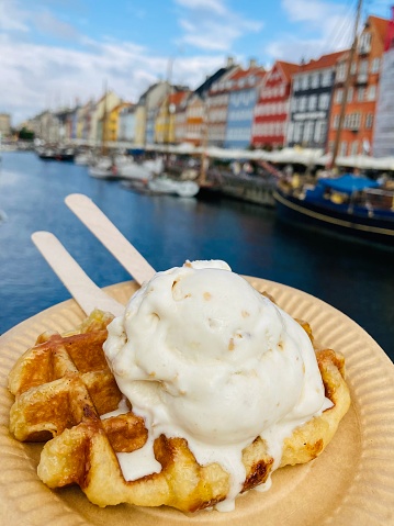 Delicious vanilla ice cream scoop on waffle with colourful houses background in Nyhavn harbour, Copenhagen, Denmark. Selective focus. Travel concept.