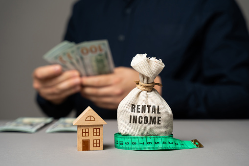 Rental income concept. The concept of profit from the rental of real estate, apartments or houses. Landlord income from housing. Money bag, miniature house and money in the hands of a businessman.
