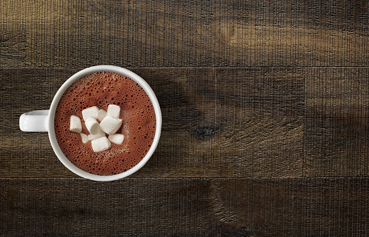 Looking down on hot chocolate mug with marshmallows on wooden table top