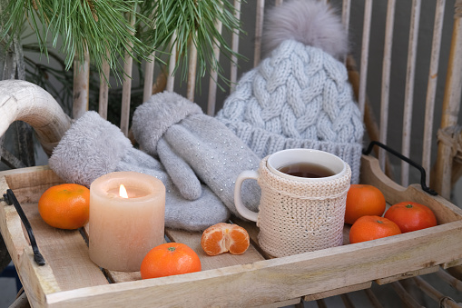 cozy woolen things, a hat and mittens, a mug of hot tea on a tray, delicious vitamin tangerines, a candle is burning, a wicker garden chair, a concept vacation, a weekend in nature