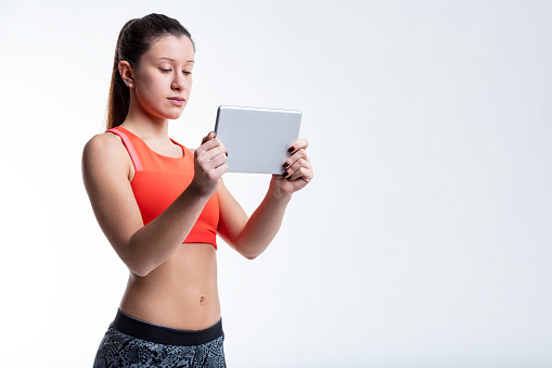 Young woman, featuring a toned flat stomach, utilizing digital devices for her workouts, embodying the idea of fitness and beauty through discipline