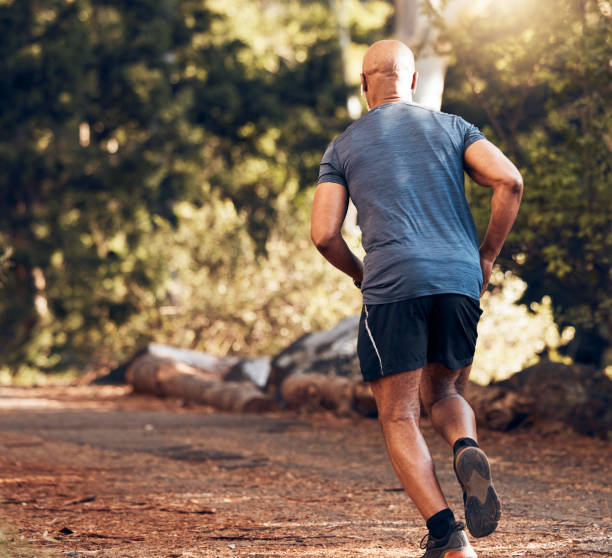 istock Back of black man running in park, nature and forest for cardio workout, exercise or training. Sports male, runner and outdoor fitness from behind for energy, healthy lifestyle and wellness in garden 1592210714