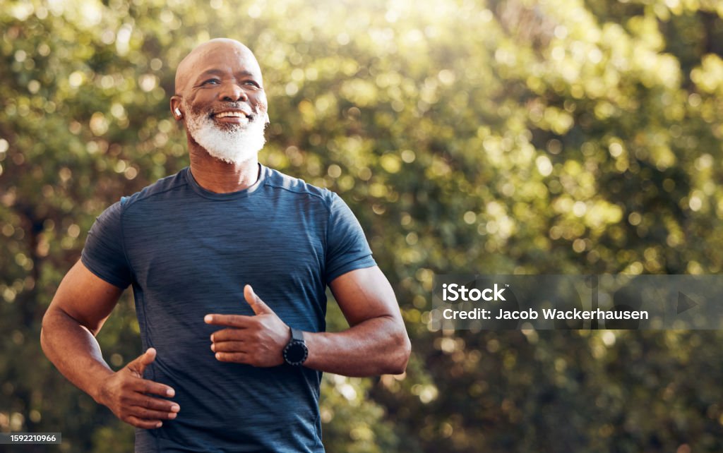Happy black man running in park with music, smile and mockup in nature, garden and workout. Senior male, outdoor runner and motivation for fitness, energy and healthy exercise training with earphones Exercising Stock Photo