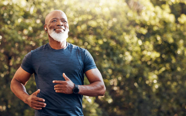 Szczęśliwy czarny człowiek biegający po parku z muzyką, uśmiechem i makietą na łonie natury, ogrodem i treningiem. Starszy mężczyzna, biegacz outdoorowy i motywacja do treningu fitness, energii i zdrowych ćwiczeń ze słuchawkami – zdjęcie