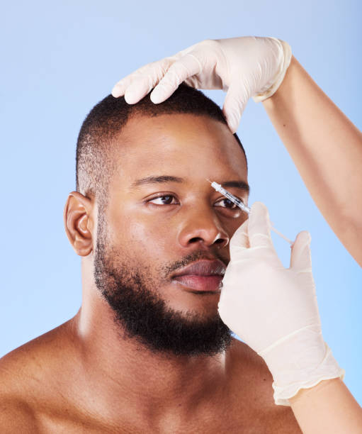 istock Black man, plastic surgery and needle in studio for beauty, dermatology or face transformation by background. African patient, model or surgeon hands for skincare, syringe or eye filler for aesthetic 1592215351