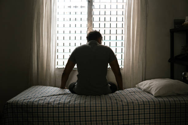 istock Desperate man in silhouette sitting on the bed alone. masculinity and emasculation concept. 1592220165