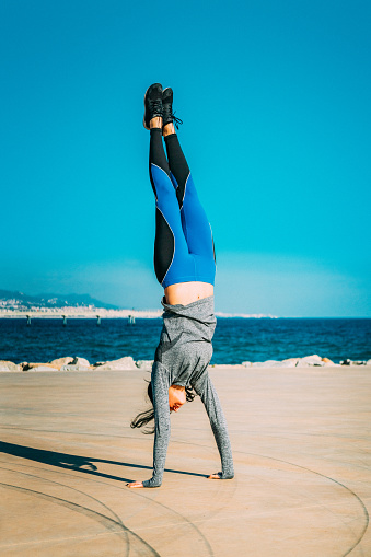 Young sporty looking woman doing handstand on beach.