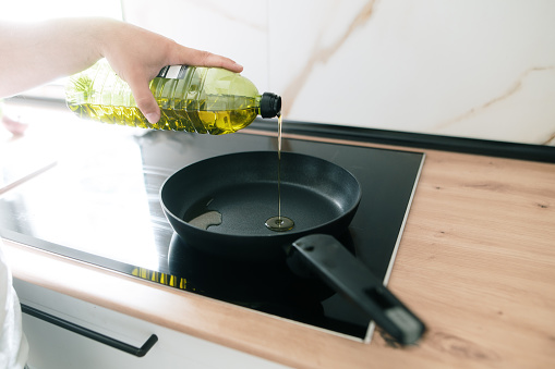 A person pouring olive oil in a frying pan on an induction stove