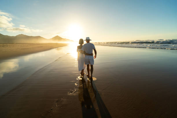 rückansicht eines romantischen pärchenspaziergangs an einem sandstrand auf der insel fuerteventura. - fuerteventura stock-fotos und bilder