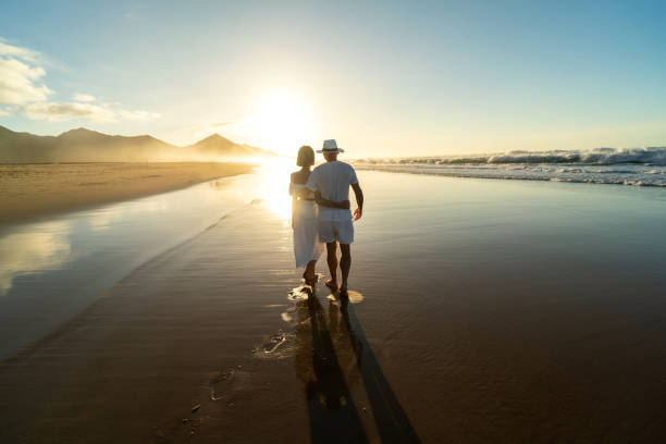 vista posteriore di coppie romantiche passeggiate lungo una spiaggia sabbiosa sull'isola di fuerteventura. - fuerteventura foto e immagini stock