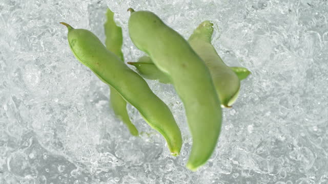 Broad Bean Pods Falling into Pot of Boiling Water Making a Splash in Slow Motion - Table Top View