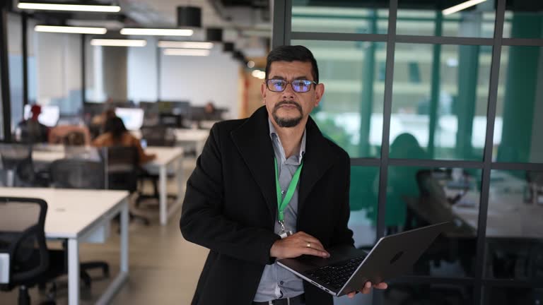 Portrait of a mature man standing working with laptop in the office