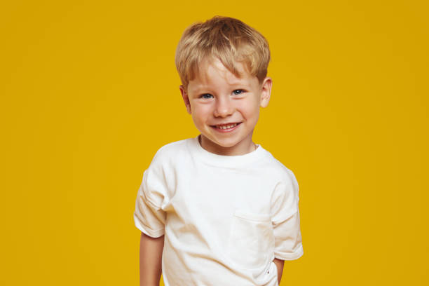 Happy little blonde male kid boy in white tshirt laughing at camera against orange background Closeup portrait of happy little blonde male kid boy in white tshirt, laughing while standing isolated on yellow background. People, childhood, lifestyle concept one little boy stock pictures, royalty-free photos & images