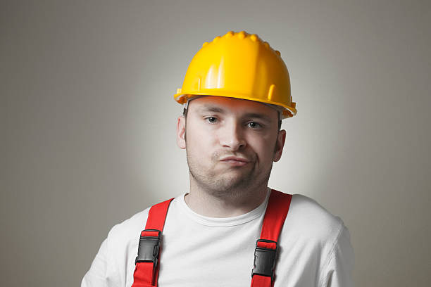 Disappointed young worker Unhappy young handyman with yellow hard hat lazy construction laborer stock pictures, royalty-free photos & images