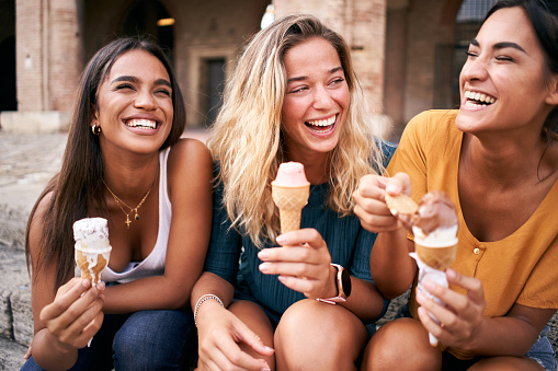 Three young woman eating ice cream cones at the touristic European Roman city on a hot summer day during their vacation. High quality photo